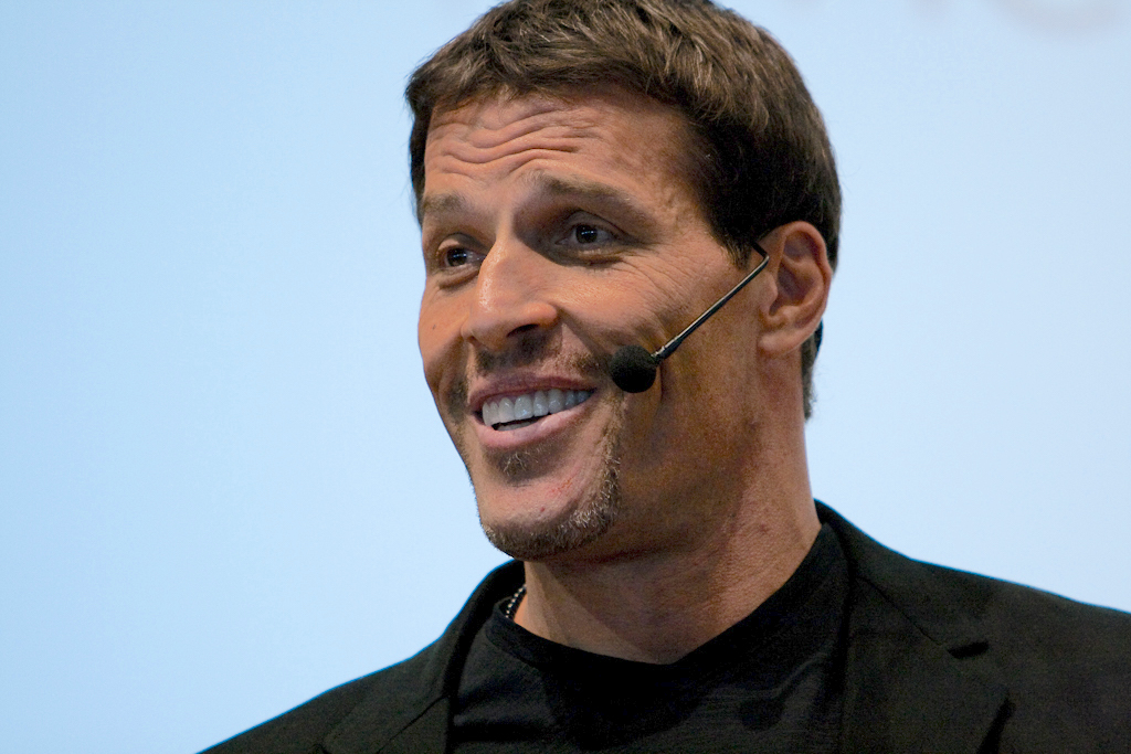 Tony Robbins hablando en un evento, con micrófono de diadema y expresión motivadora. Foto de Randy Stewart, CC BY-SA 2.0 https://creativecommons.org/licenses/by-sa/2.0, via Wikimedia Commons.